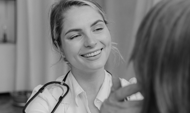 A smiling female healthcare professional with a stethoscope around her neck talking to a patient in a medical setting.