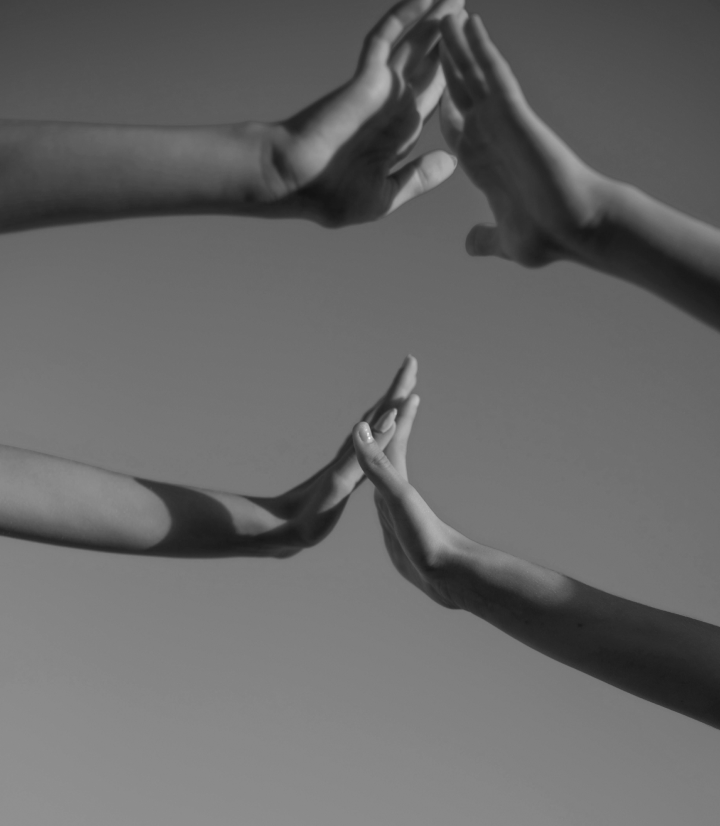 Black and white photo of multiple hands reaching out and touching in a series of high fives or hand gestures against a plain background.