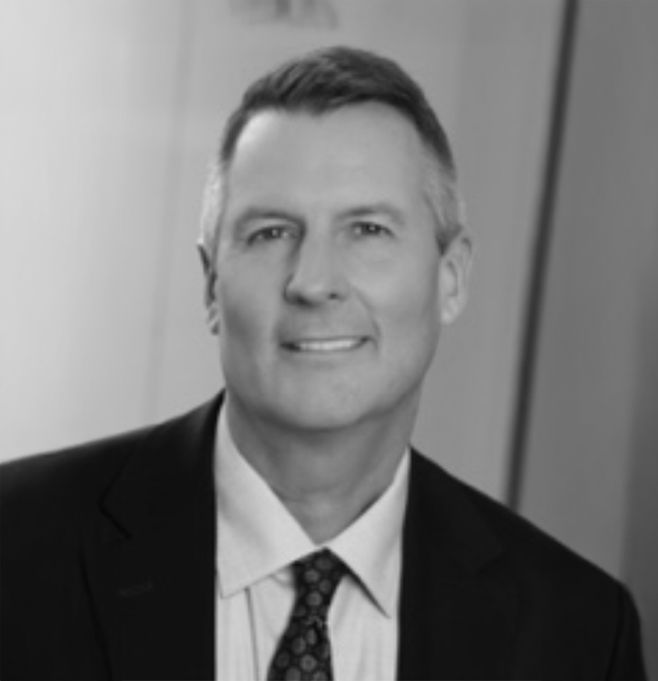 Black and white headshot of a man in a suit with short hair, smiling, against a blurred background.
