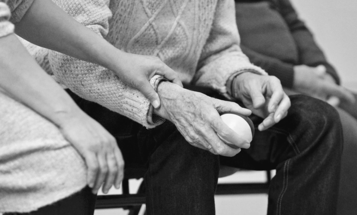 Close-up of an elderly person's hands holding a cane, with another person hand resting on top.