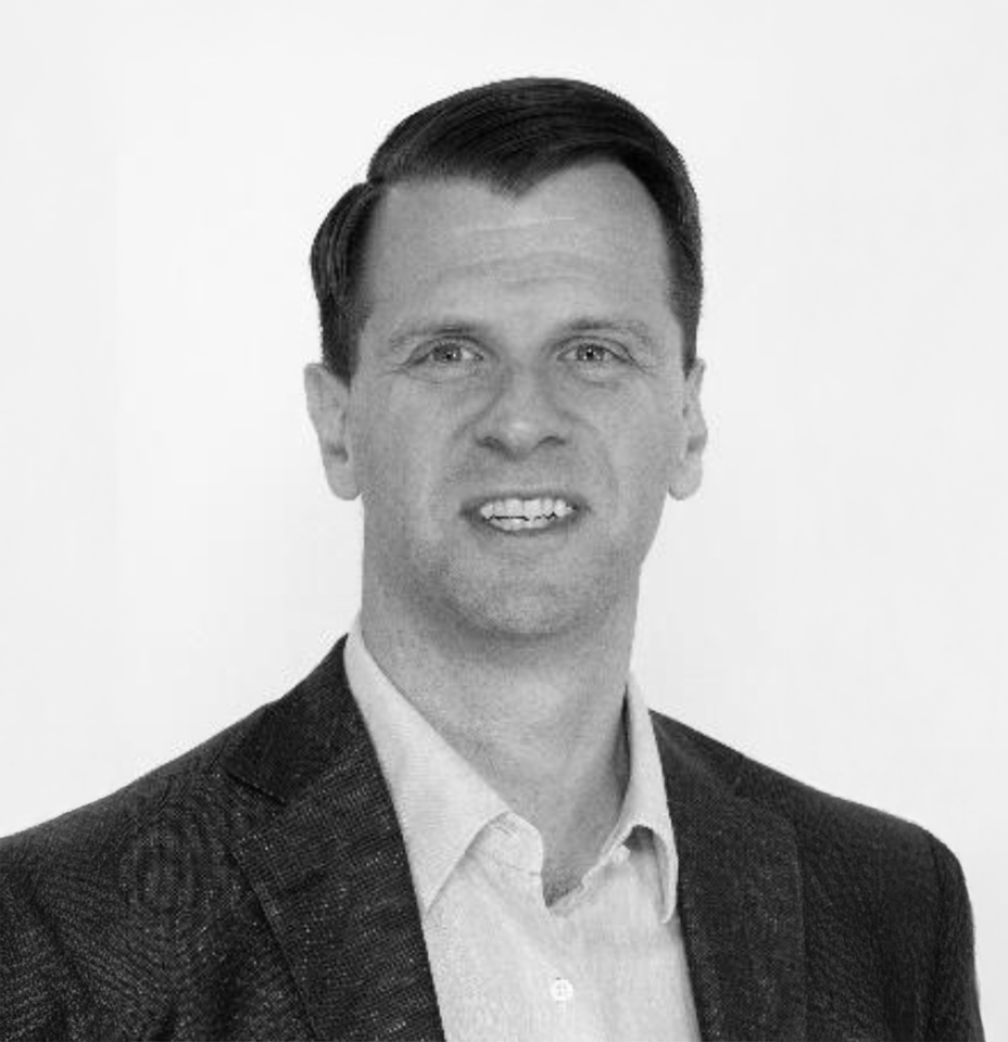 Black and white portrait of a smiling man with dark, neatly combed hair, wearing a dark blazer and light-colored shirt, against a plain white background.