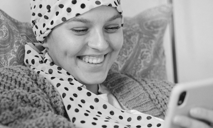 A woman with a polka dot headscarf smiling while looking at her phone.