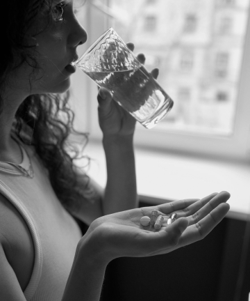 A woman drinking a glass of water while holding pills in her hand.