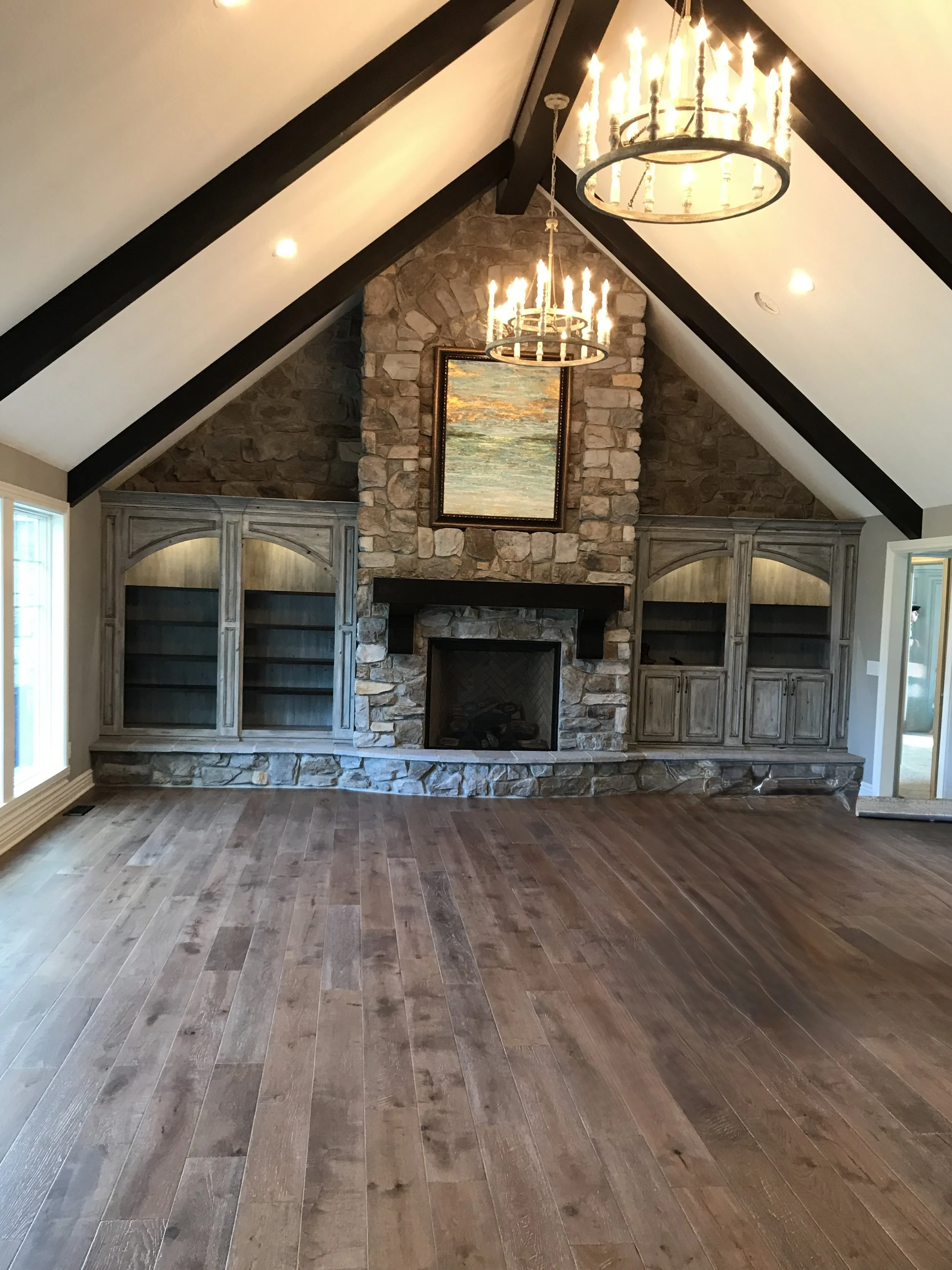 Living room with a fireplace, stone walls, wooden floors, built-in cabinets, and chandeliers hanging from a vaulted ceiling.