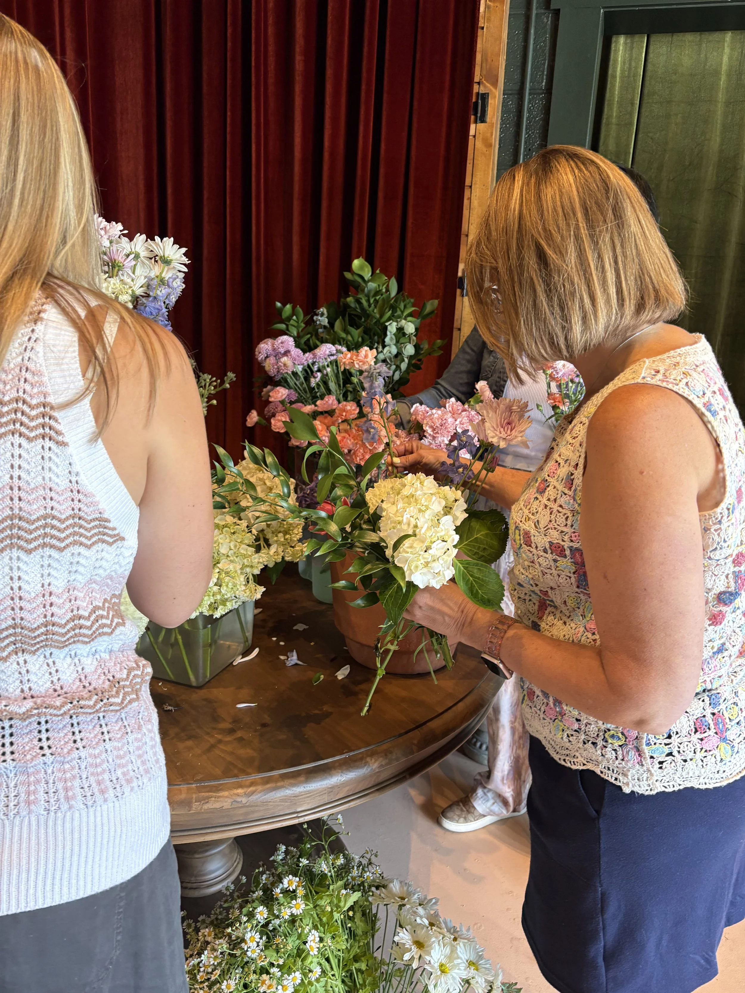 People looking at and arranging flower arrangements in a room with dark wood and green walls.