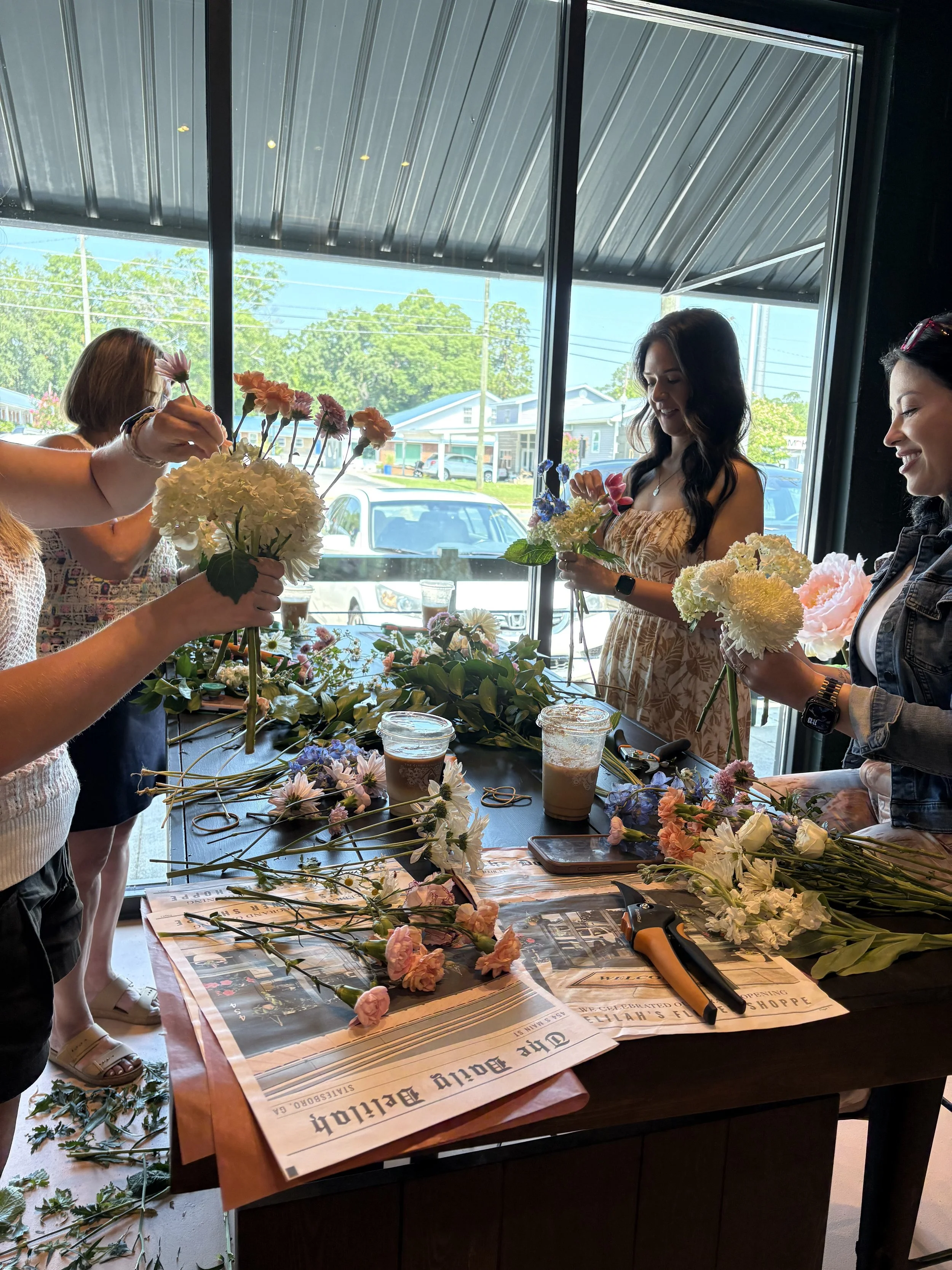 Group of women arranging flowers at a table inside a flower shop during a bouquet making class.