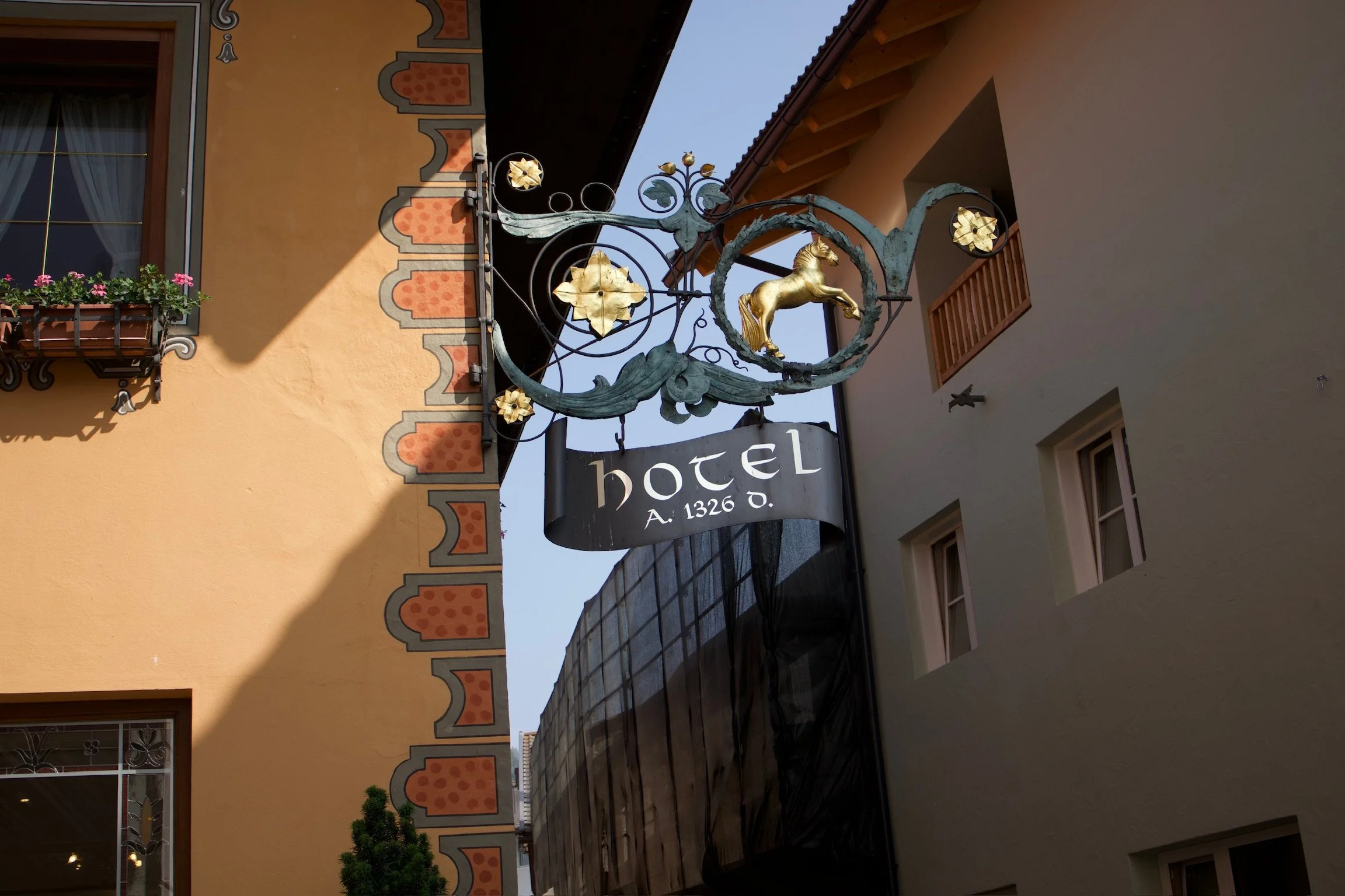 Sign hanging between buildings with a gold unicorn and decorative elements, indicating a hotel established in 1326.