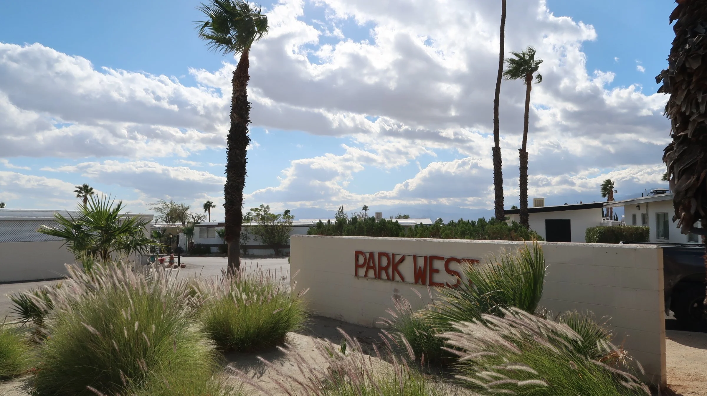 A street sign reading  Park West MHP next to landscaped plants including grasses and palm trees, in desert hot springs, ca