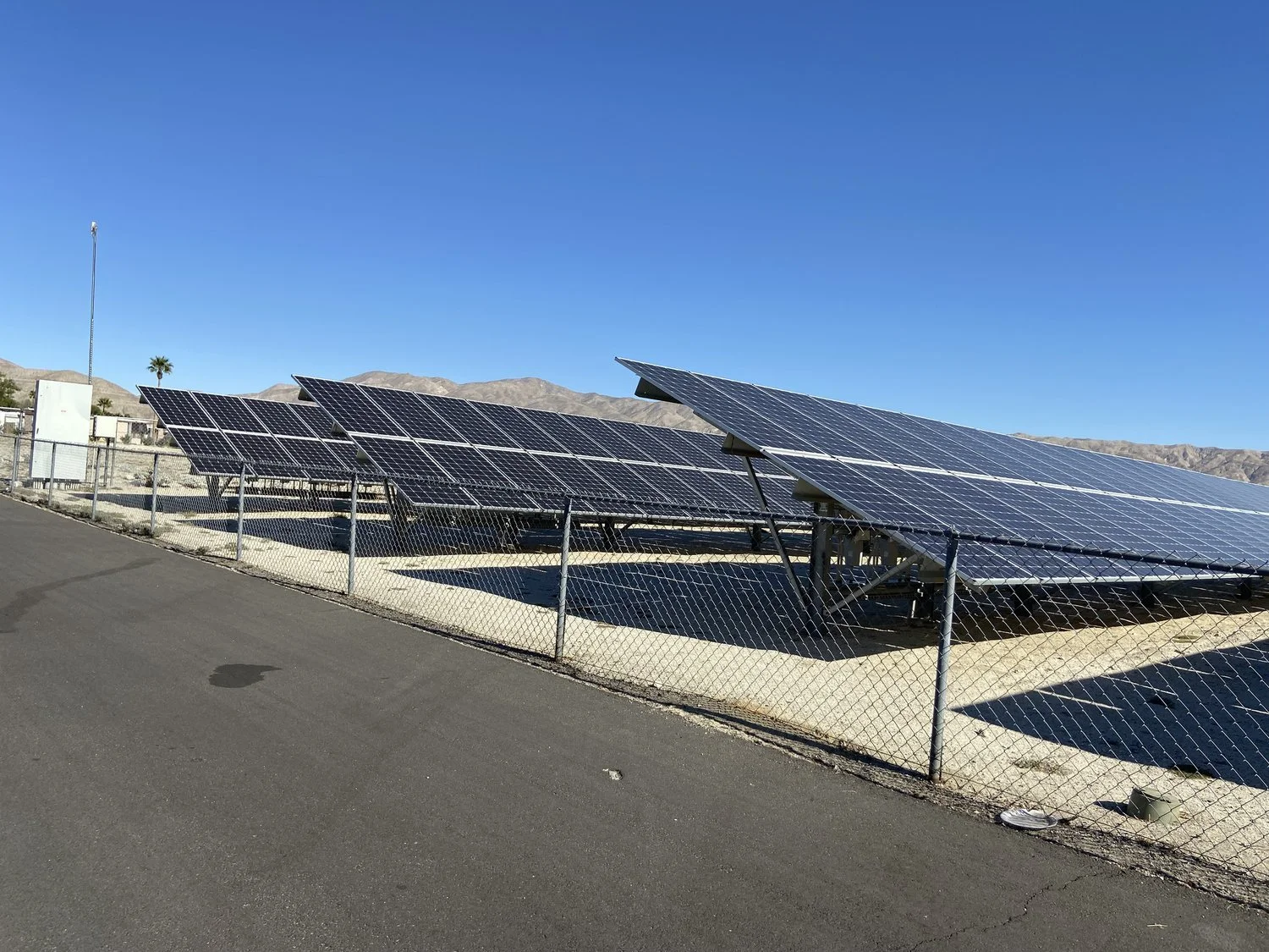 Solar panels in a fenced area on a sunny day, with mountains in the background.