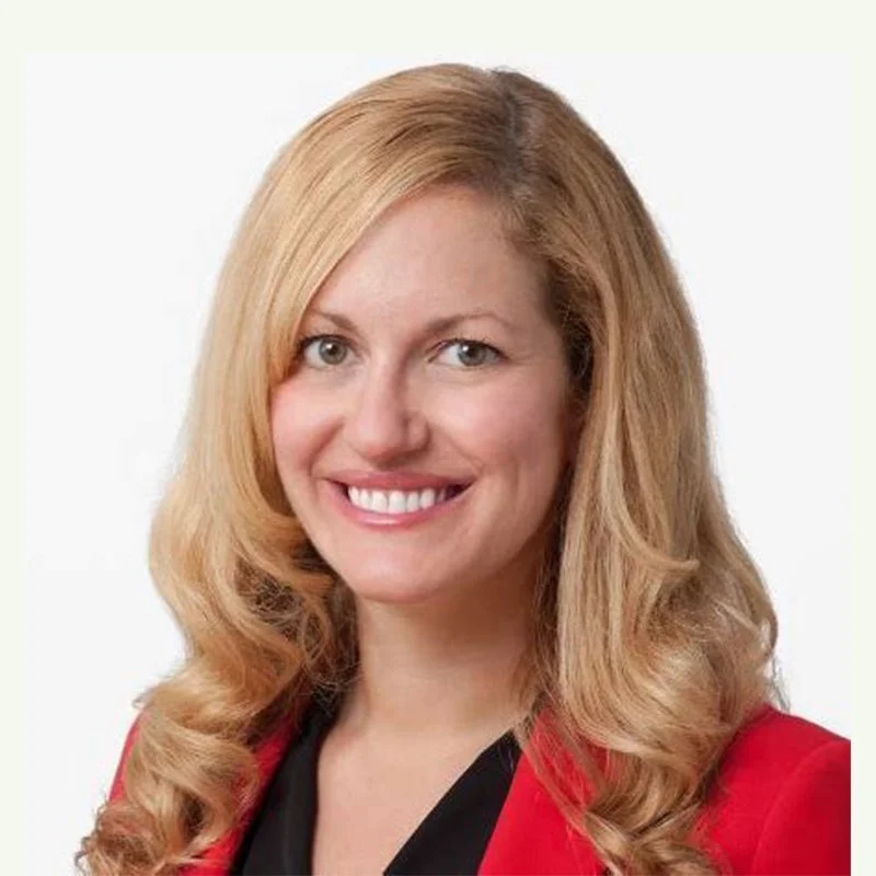 A woman with long, wavy blonde hair smiling, wearing a red blazer over a black top.