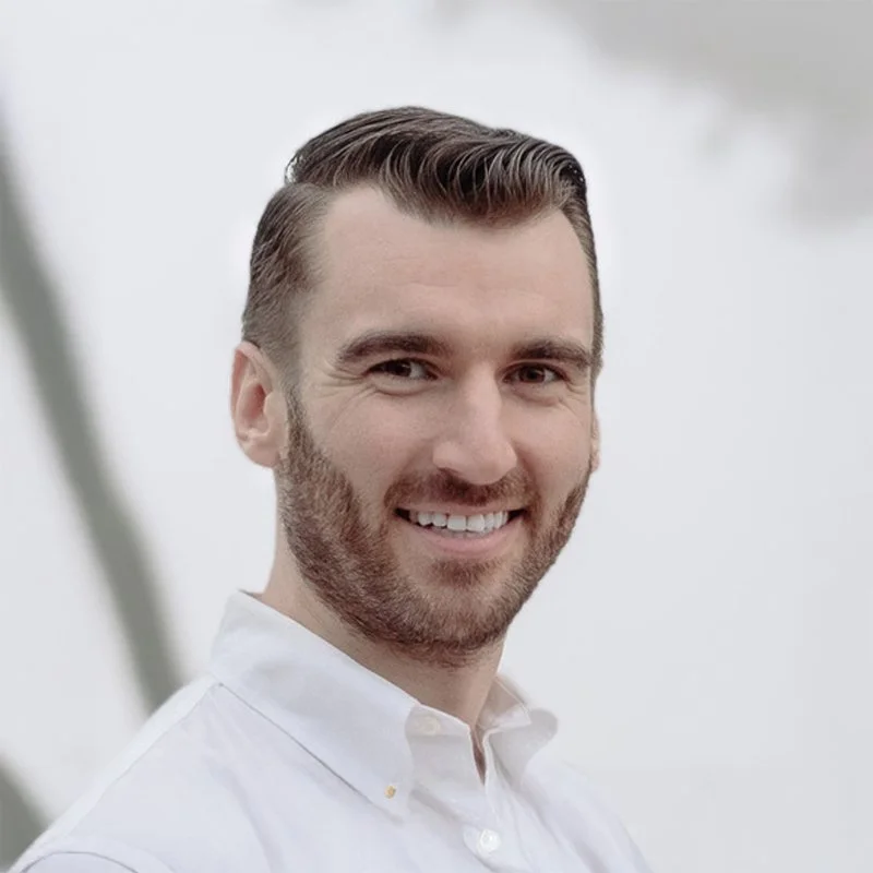 Portrait of a smiling man with short, neatly styled hair and a beard, wearing a white dress shirt.