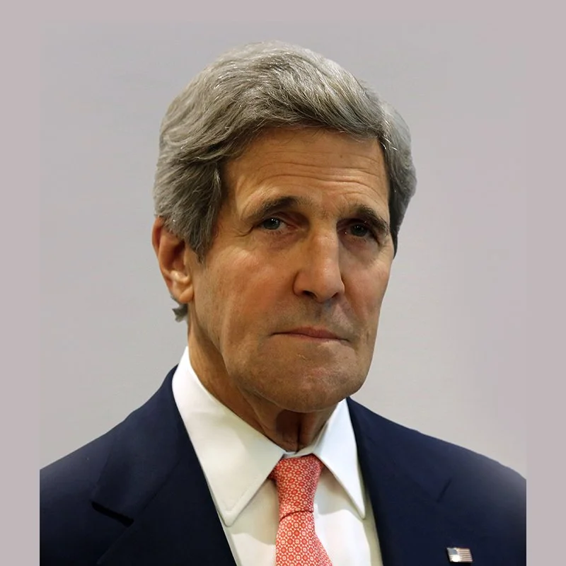Portrait of a middle-aged man with gray hair, wearing a dark suit, white shirt, and pink tie, against a plain background.