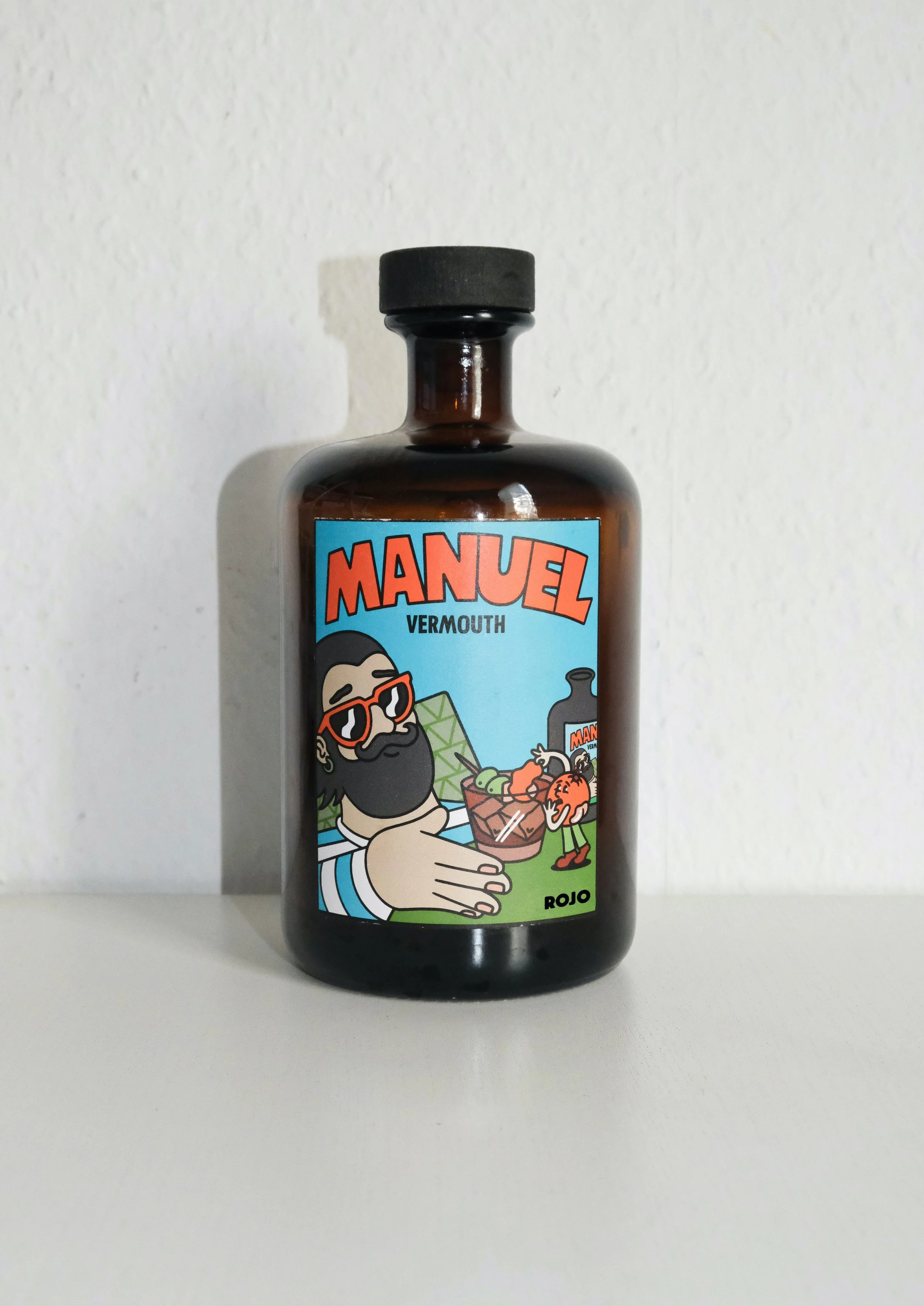 Brown bottle with a colorful label featuring cartoon characters, one holding a cocktail glass, and the words "MANUEL VERMOOTH ROJO".