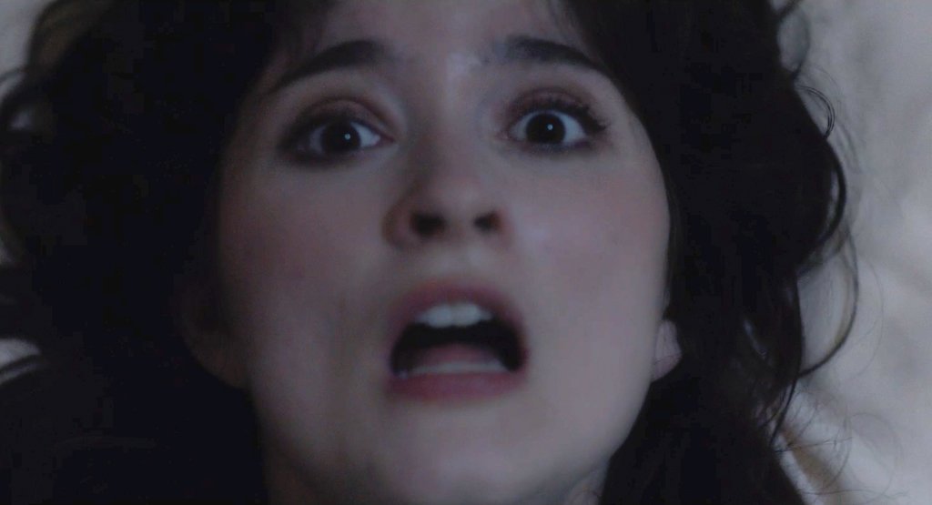 A close-up of a person looking upwards with an expression of shock or fear, mouth open and eyes wide, against a blurred background.