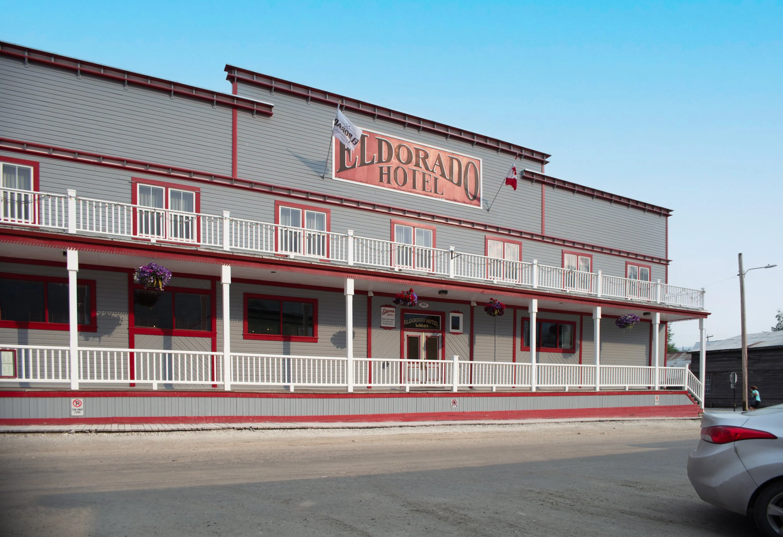 The Elderado Hotel building with a gray exterior, red trim, and white railings, with a large sign that reads 'Elderado Hotel' on the upper part of the building, and a Canadian flag hanging from the side.