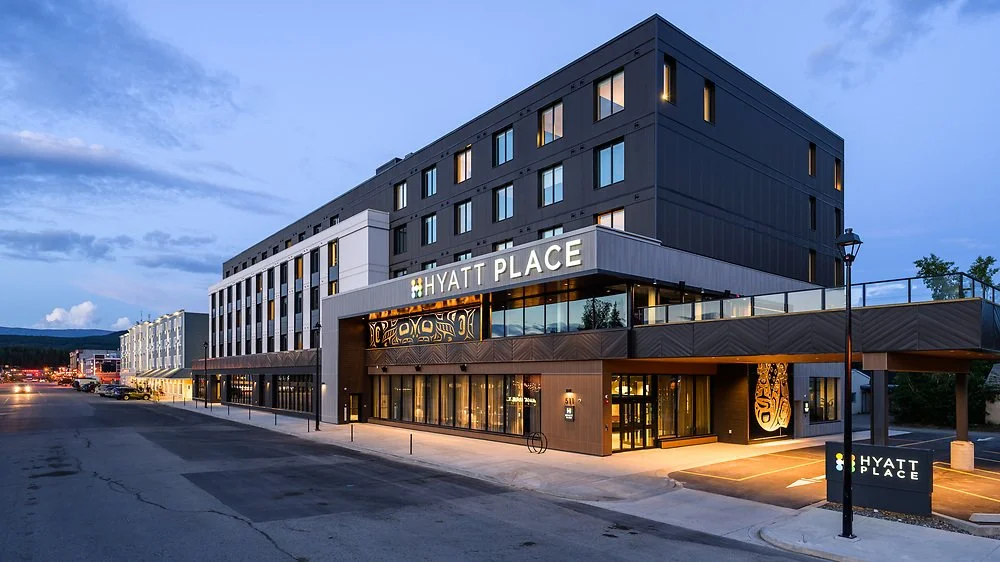 Exterior of a modern, multi-story Hyatt Place hotel building at dusk, with illuminated signage and a parking lot in the front.