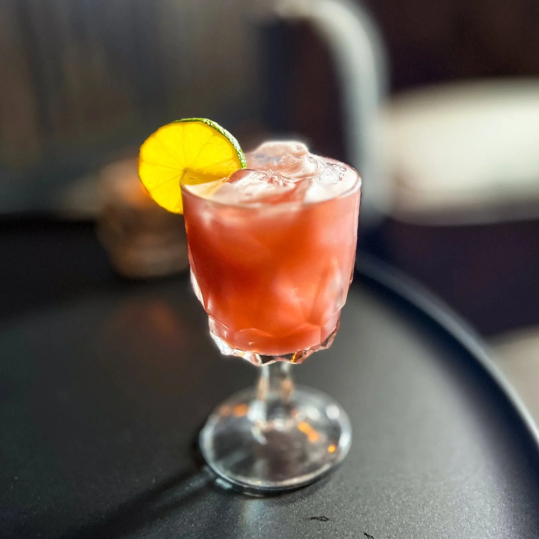A cocktail in a glass with a lemon slice garnish, filled with ice and a pinkish-red liquid.