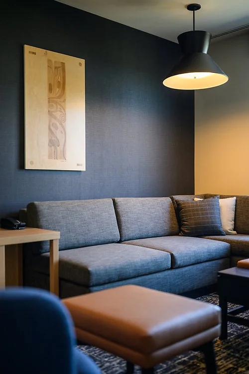 Modern living room with a grey sofa, a black wall-mounted lamp, and a piece of abstract artwork on the wall.
