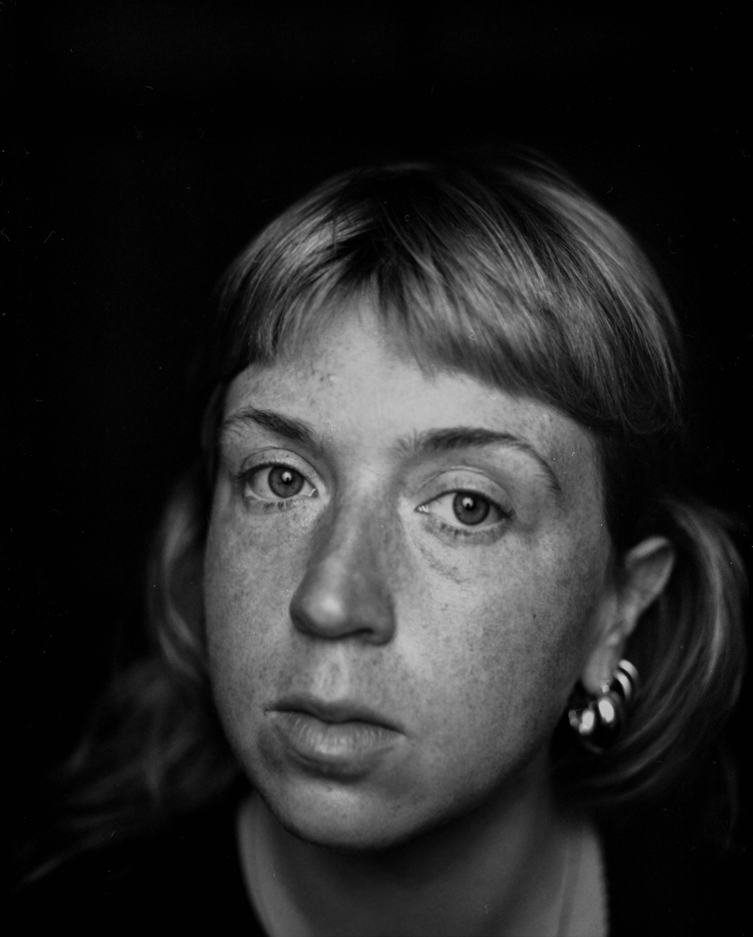 Black and white portrait photograph of a woman with short hair, light eye color, and wearing earrings, looking directly at the camera.