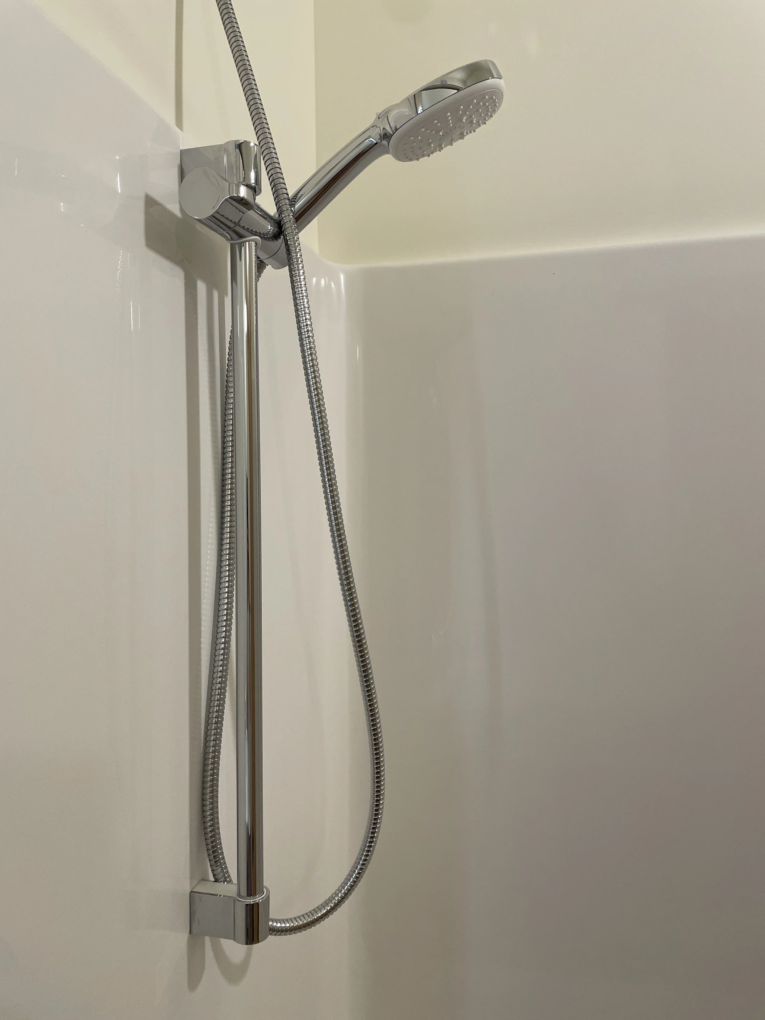 A modern showerhead attached to a flexible metal hose, mounted on a wall with a brass or gold-toned fixture.