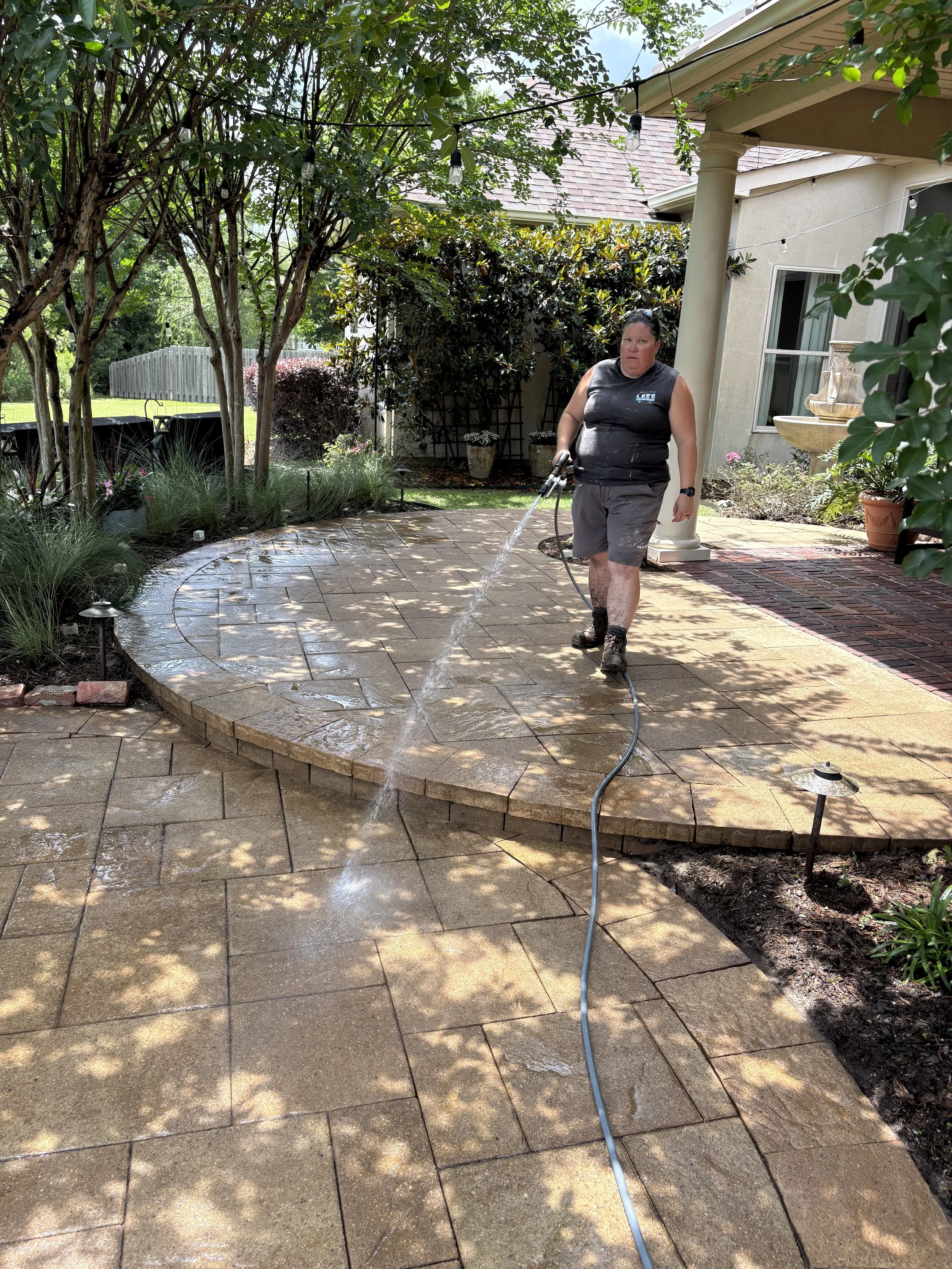 A professional technician washing a large, multi-level stone paver patio during an outdoor living space restoration service in Madisonville, LA.