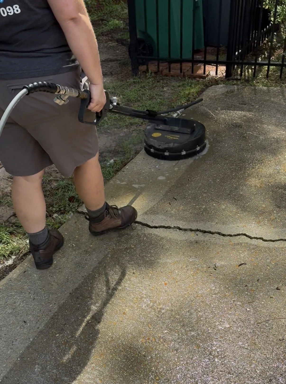 A technician using a professional surface cleaner to remove dirt, algae, and mold from a concrete driveway in Covington, LA.