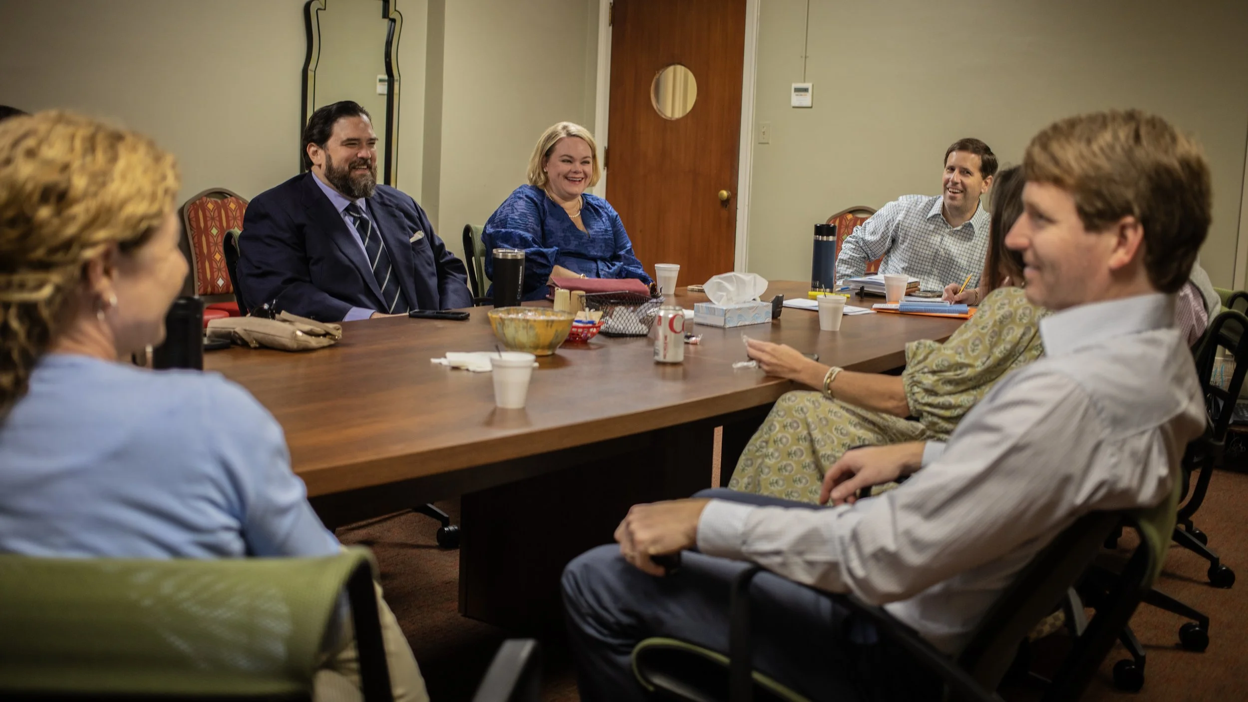 People sitting around a conference table, smiling and engaging in a Sunday School class.
