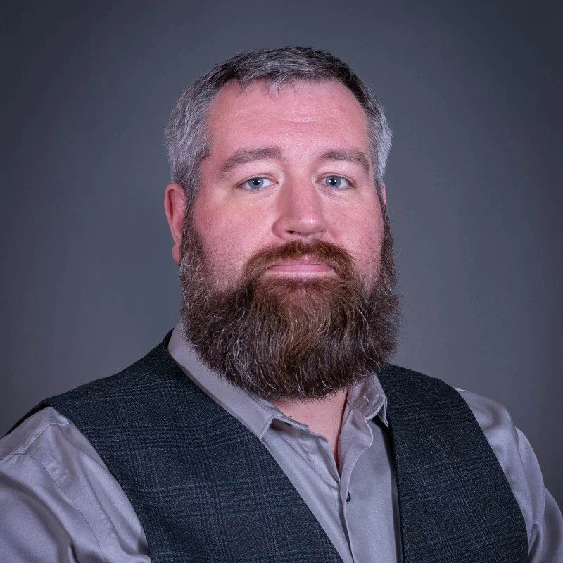 Male therapist with a beard wearing a button down shirt and a vest.
