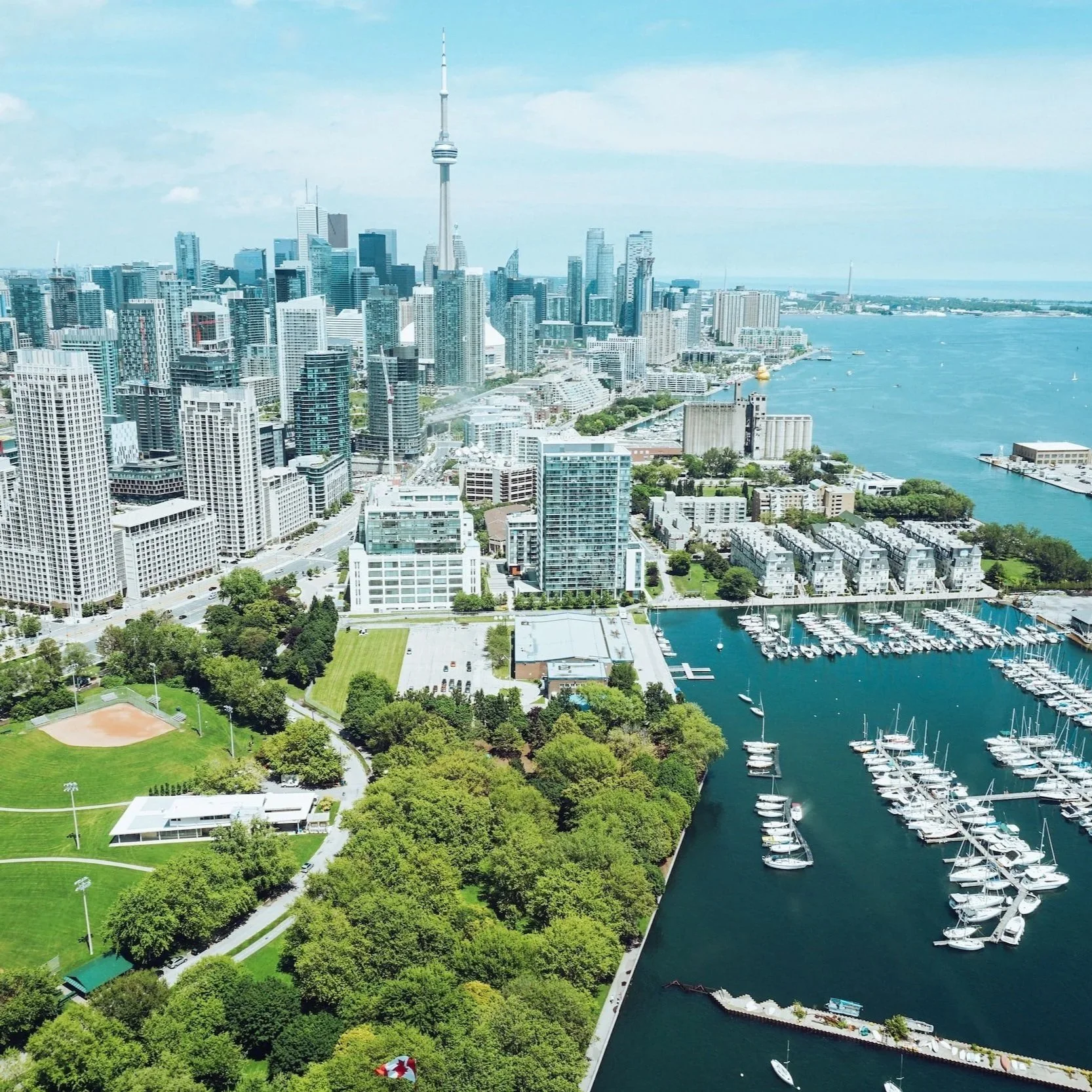 A city skyline with tall buildings, a large body of water, and a marina with boats, as seen from an aerial view.
