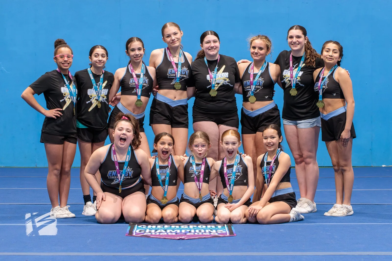 A group of cheerleaders posing with medals in front of a blue wall.