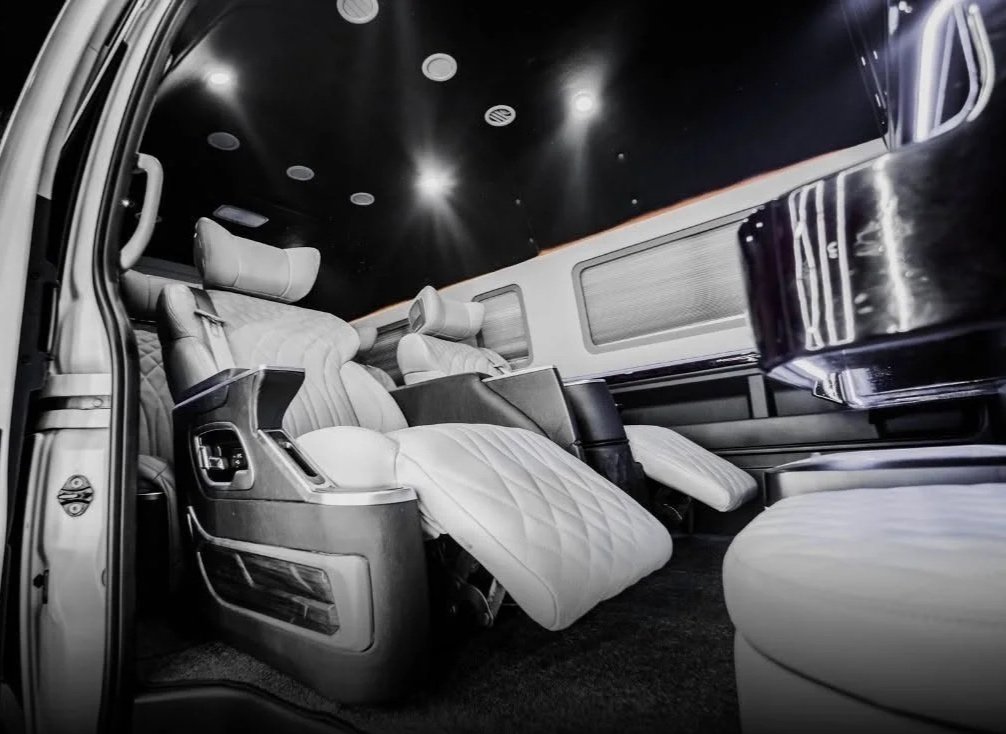 Luxury vehicle interior with plush, quilted armchair seating, headrests, and ambient ceiling lighting.