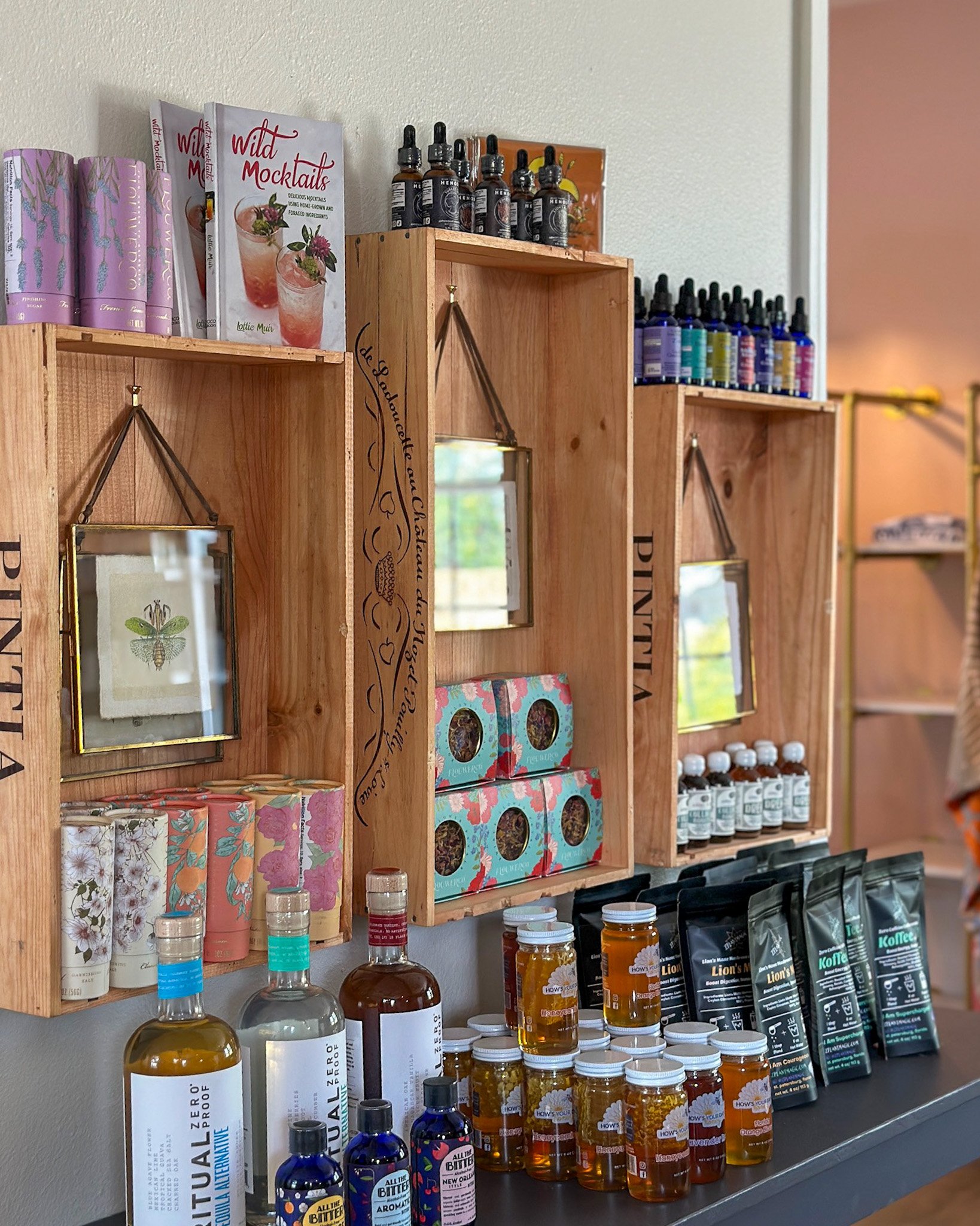 Wooden wall shelves displaying a curated mix of wellness products – including herbal tinctures, honey jars, books on holistic living, and other natural lifestyle goods.