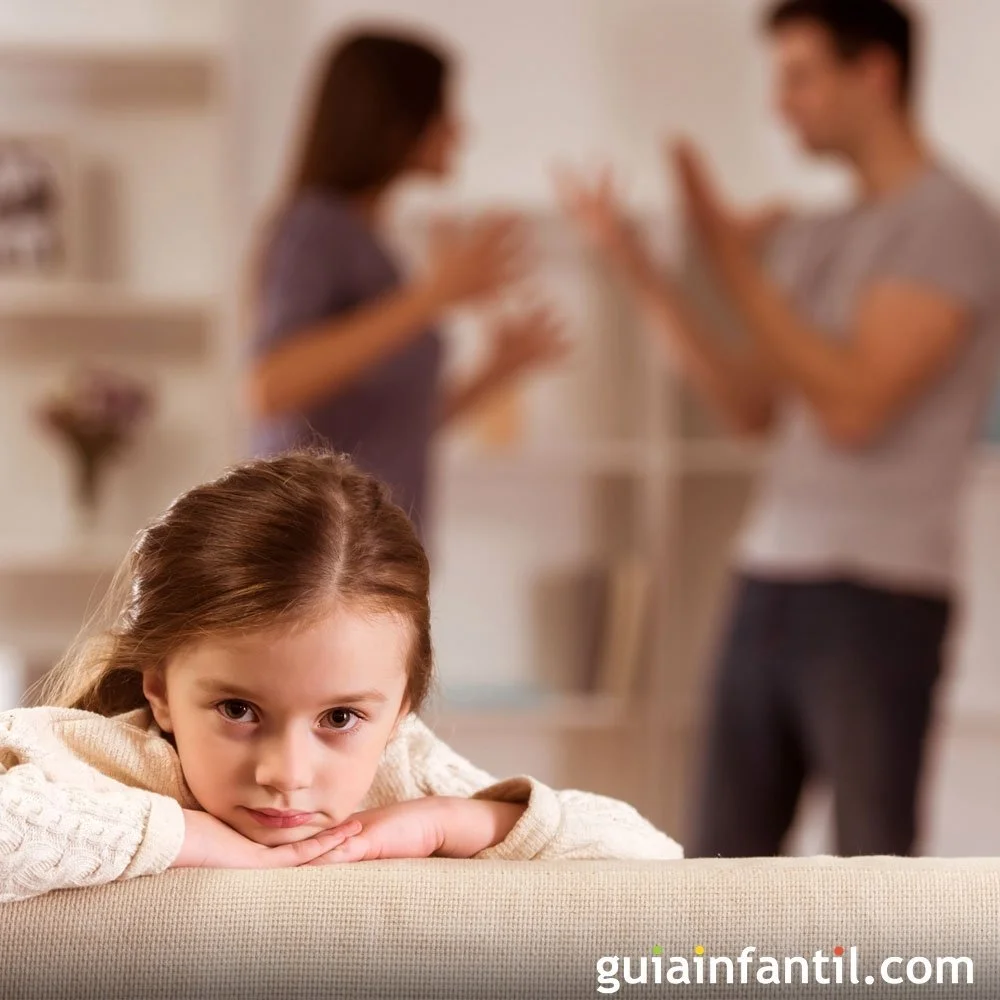 Una niña de cabello castaño claro y expresión triste, apoyando su rostro sobre sus manos, en un ambiente de interior. En el fondo, unos adultos discuten de manera tensa, pero están desenfocados.
