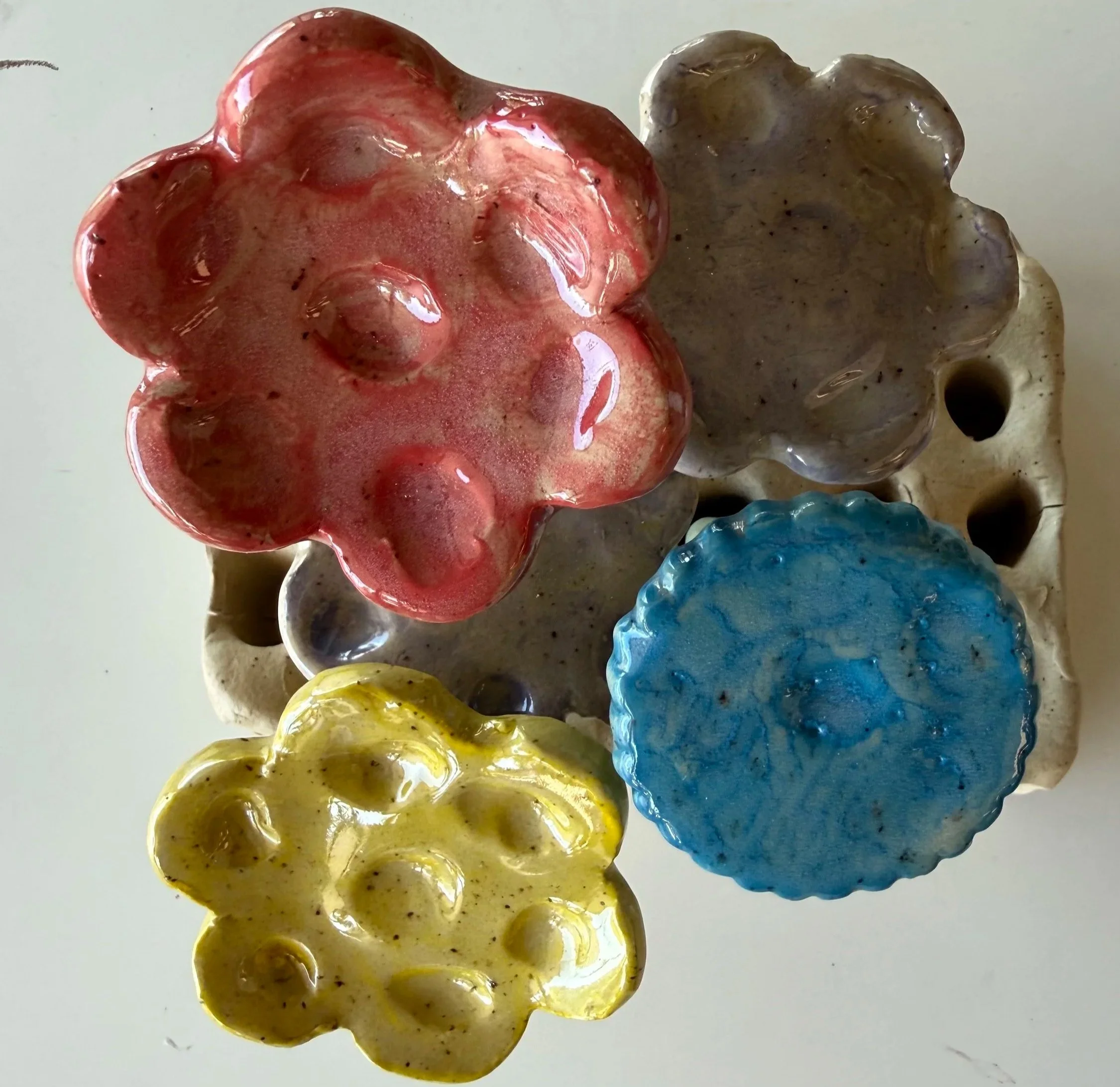 Colorful ceramic or glass animal figurines arranged in a row, featuring red, brown, blue, yellow, and other colors, with a glossy finish.