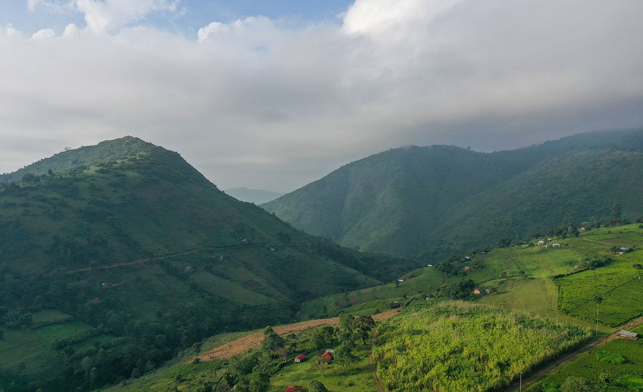 Green mountains and hills with small farmhouses and fields under a cloudy sky.