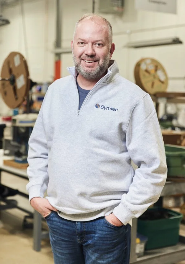 Man in gray Symtec sweatshirt smiling in workshop