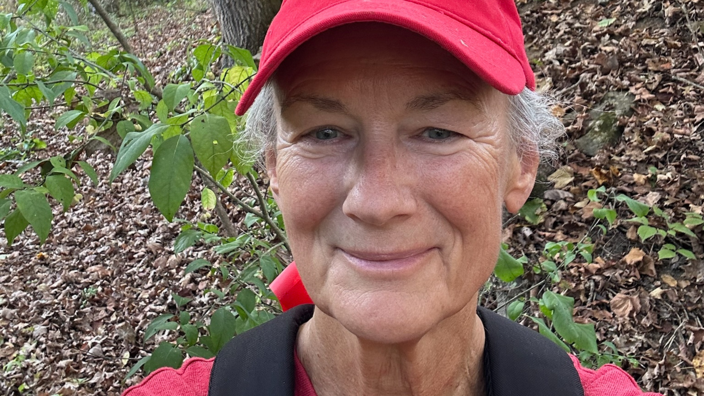 Mackey wearing a red hat and backpack outside in a forest