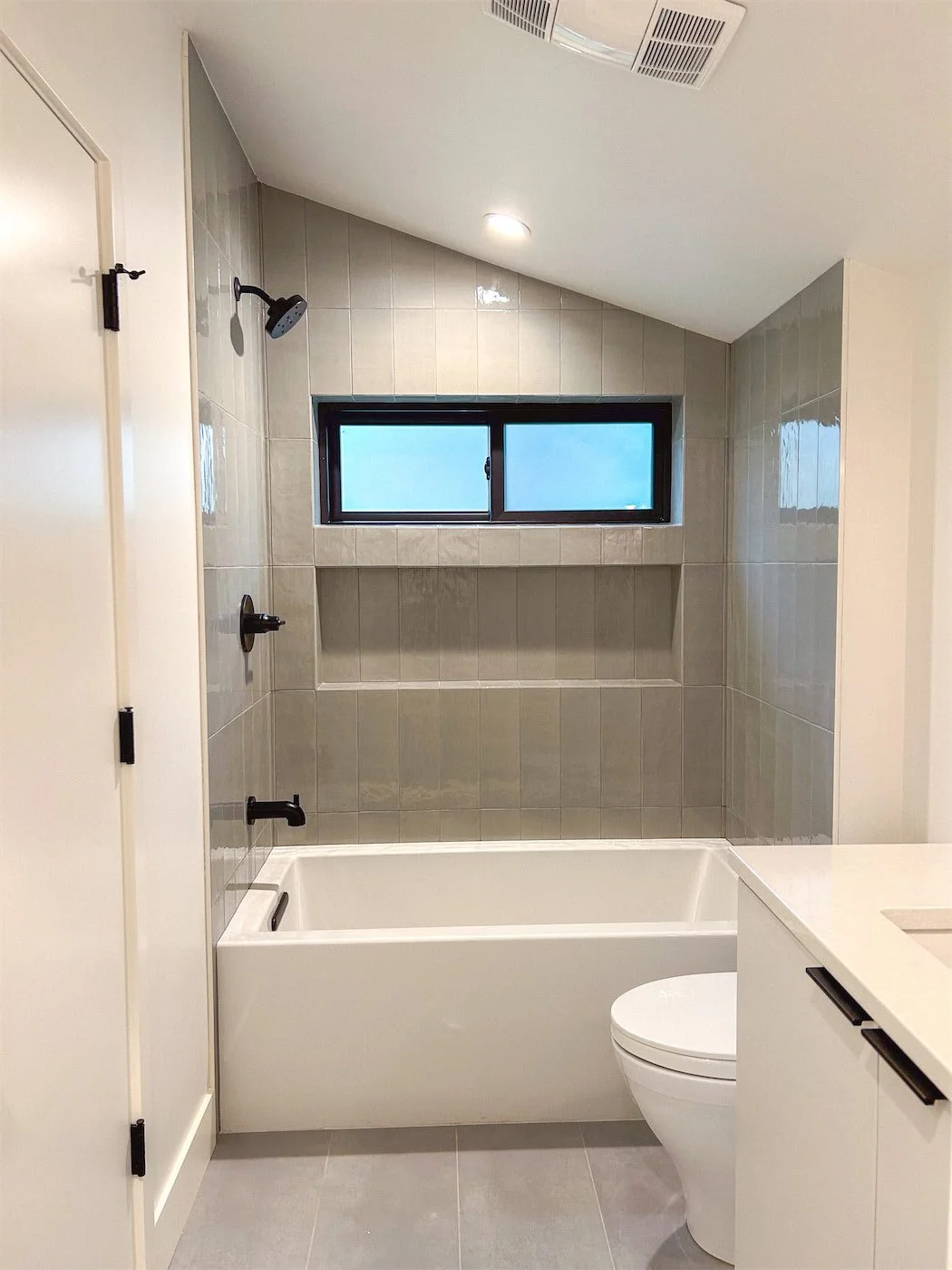 Modern bathroom with bathtub, toilet, beige tiled walls, and frosted window.