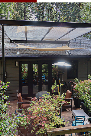 Outdoor patio area with a mesh canopy, chairs, and dining furniture, surrounded by greenery and trees.