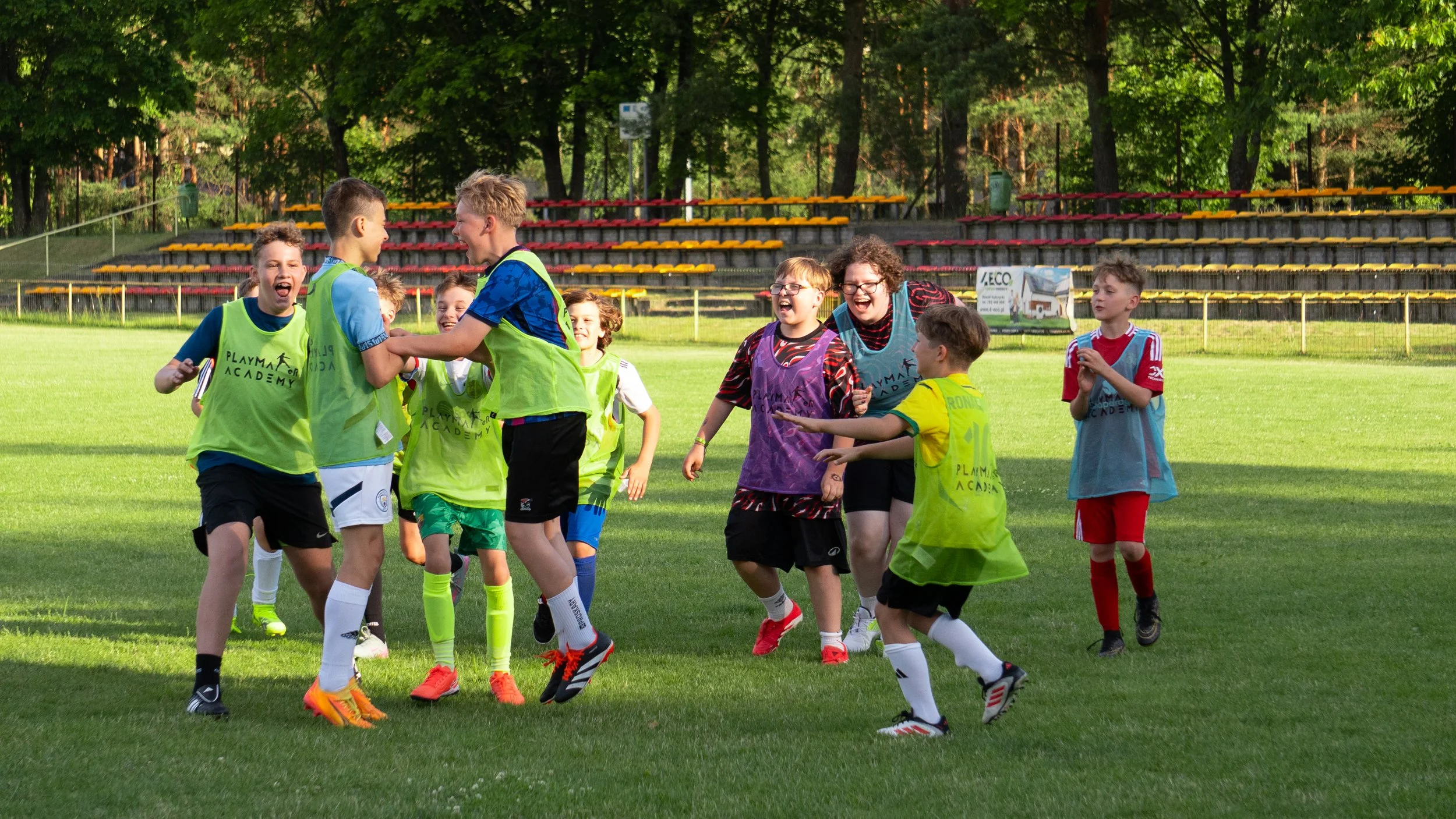 A group of people on an outdoor sports field celebrating, with one person kneeling and high-fiving a child holding a soccer ball.