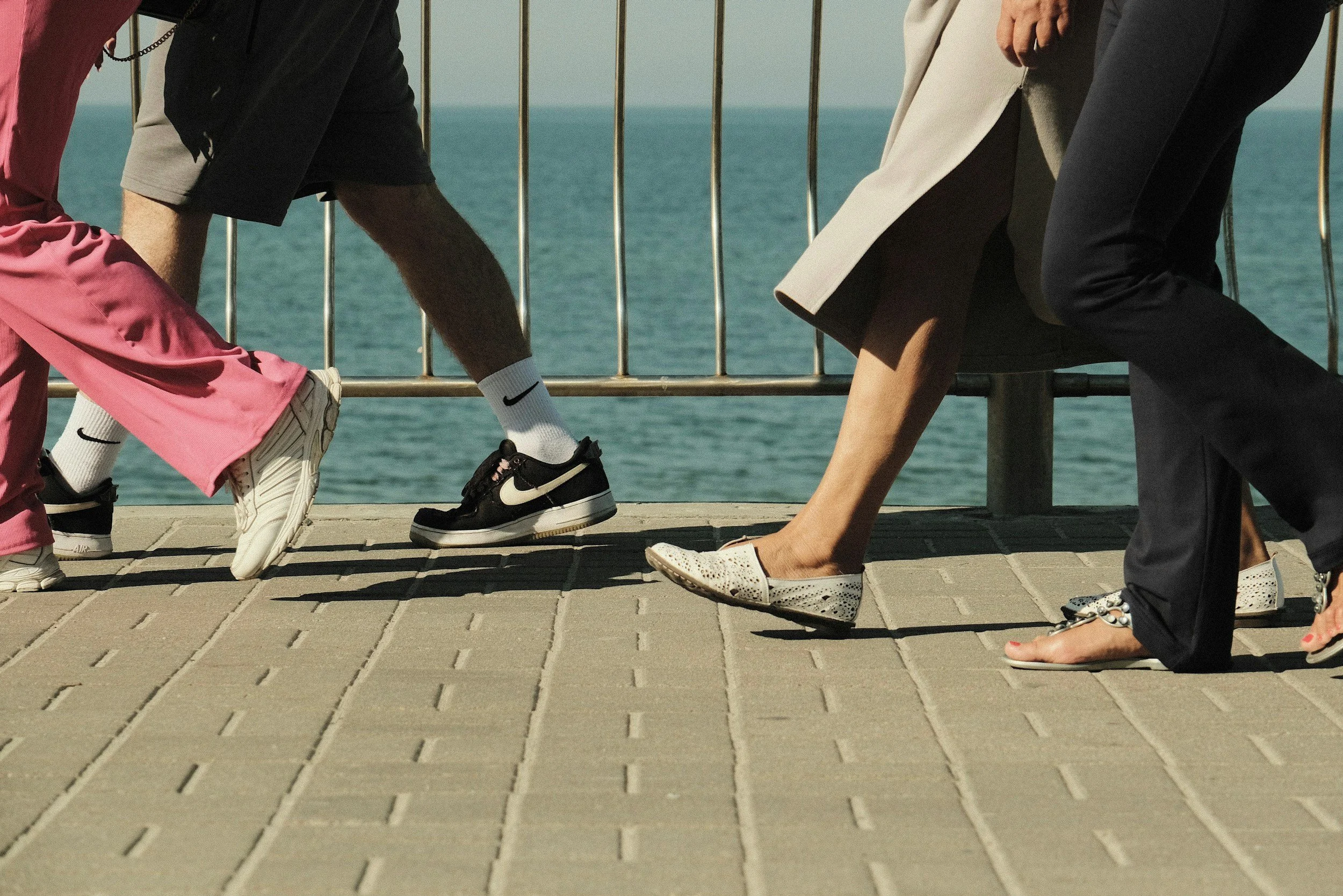 A group of people stretching or warming up outdoors on a paved walkway near a body of water, with an ocean in the background. Some are headed out to their next job.