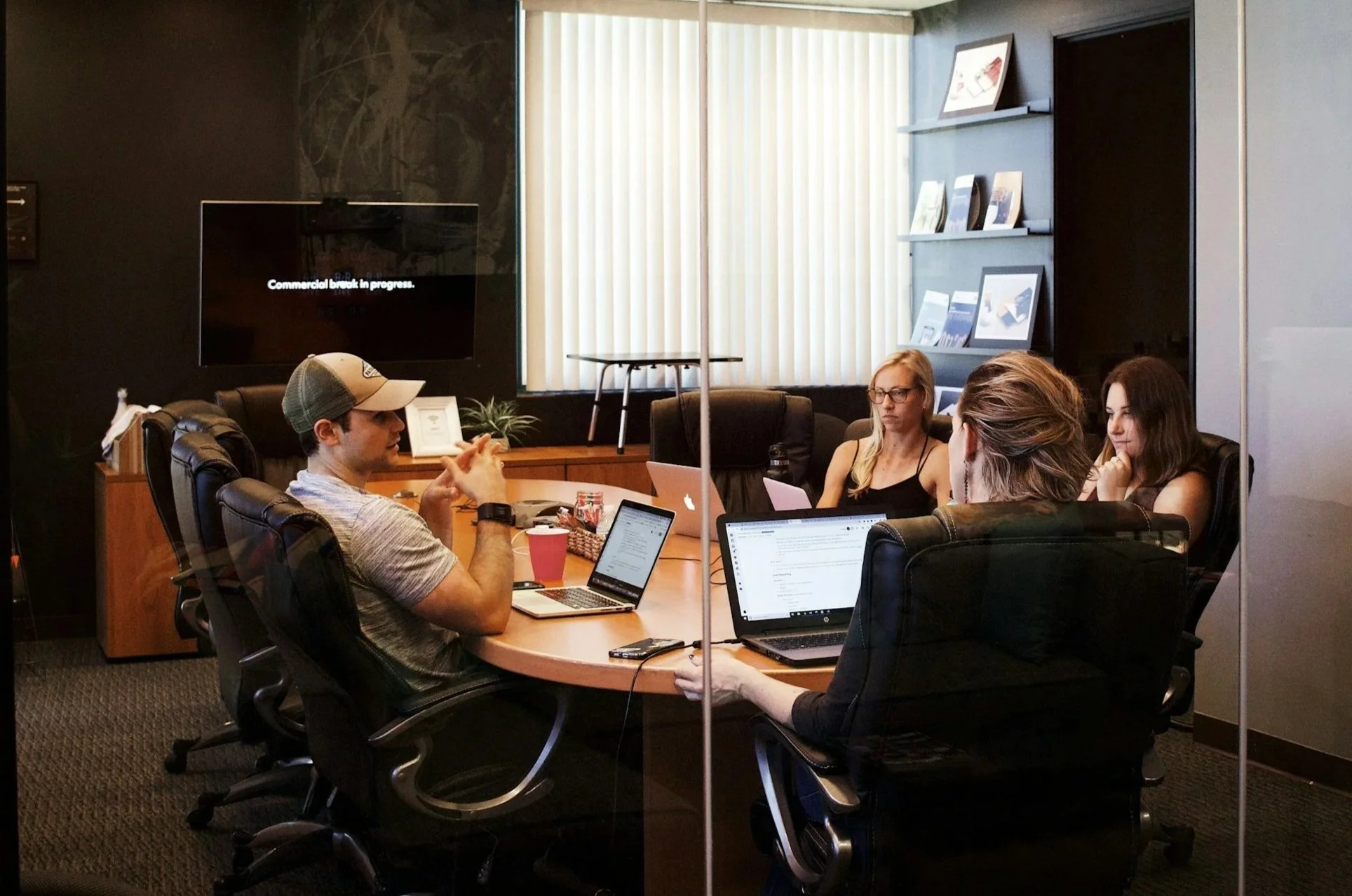 People seated around a conference table during a meeting in an office. One person is working on a laptop, and others are listening or looking at their screens. They received help from Career Evolution.