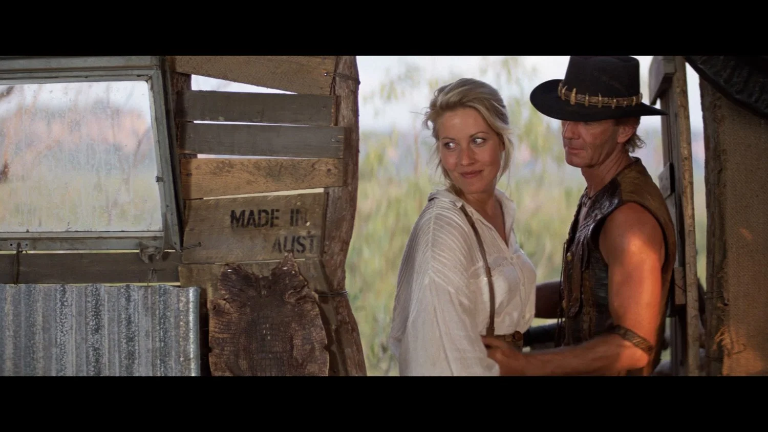 Mick Dundee ( Actor Paul Hogan ) and Sue Charlton Actor ( Linda Kozlowski ) stand close together inside Micks rustic wooden shelter in the Australian Outback.