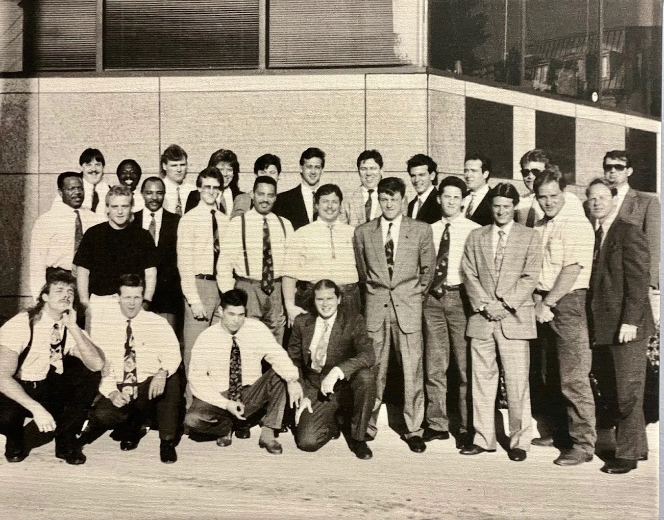 Black and white photo of a group of young men and women in business attire standing outside a building, posing for a group picture.