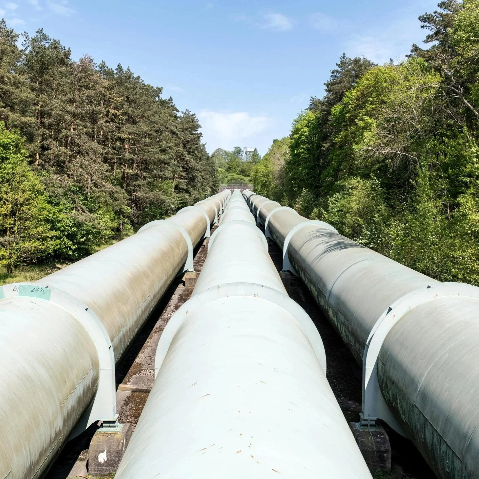 Three large oil pipelines stretching into the distance across an open landscape, emphasizing their length and industrial scale.