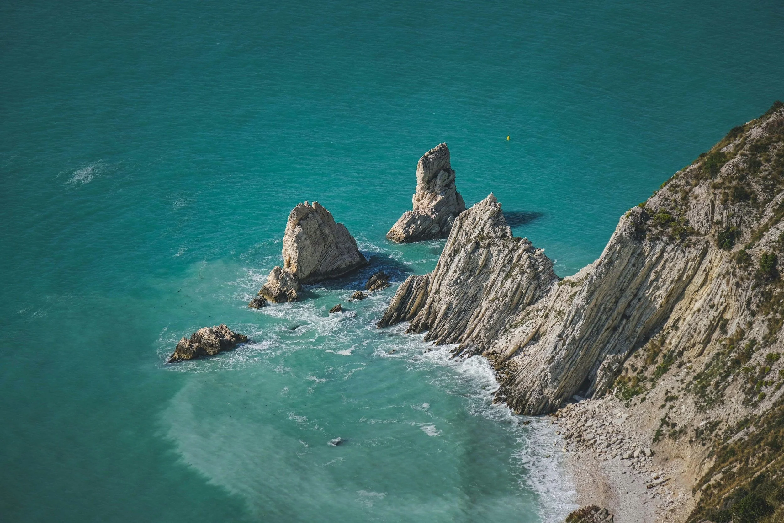 View looking down from a rocky cliff onto a deep blue ocean, with rugged rocks and waves visible along the seaside below.