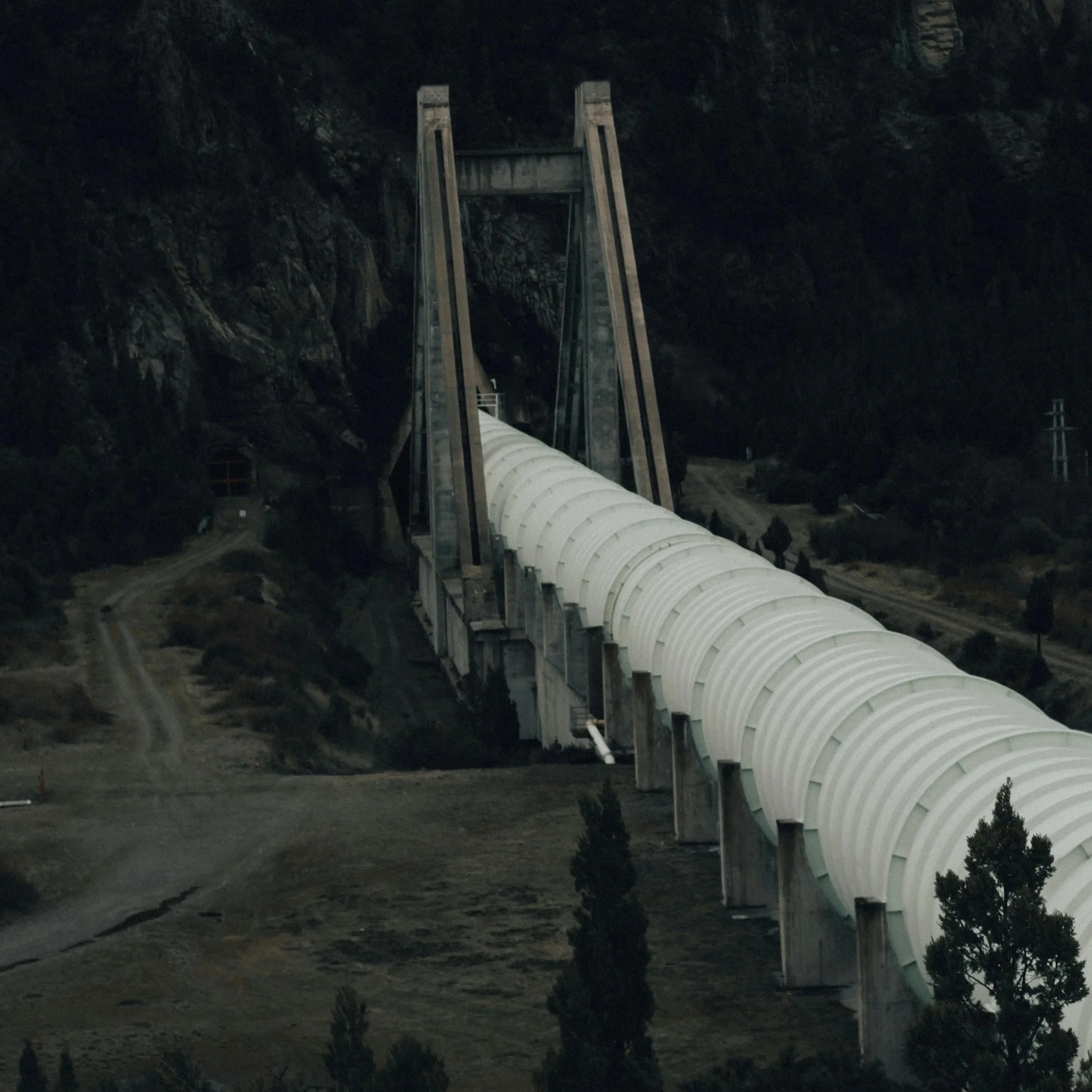 Large white pipeline with a very wide diameter stretching across a rugged landscape, highlighting its scale and industrial presence.