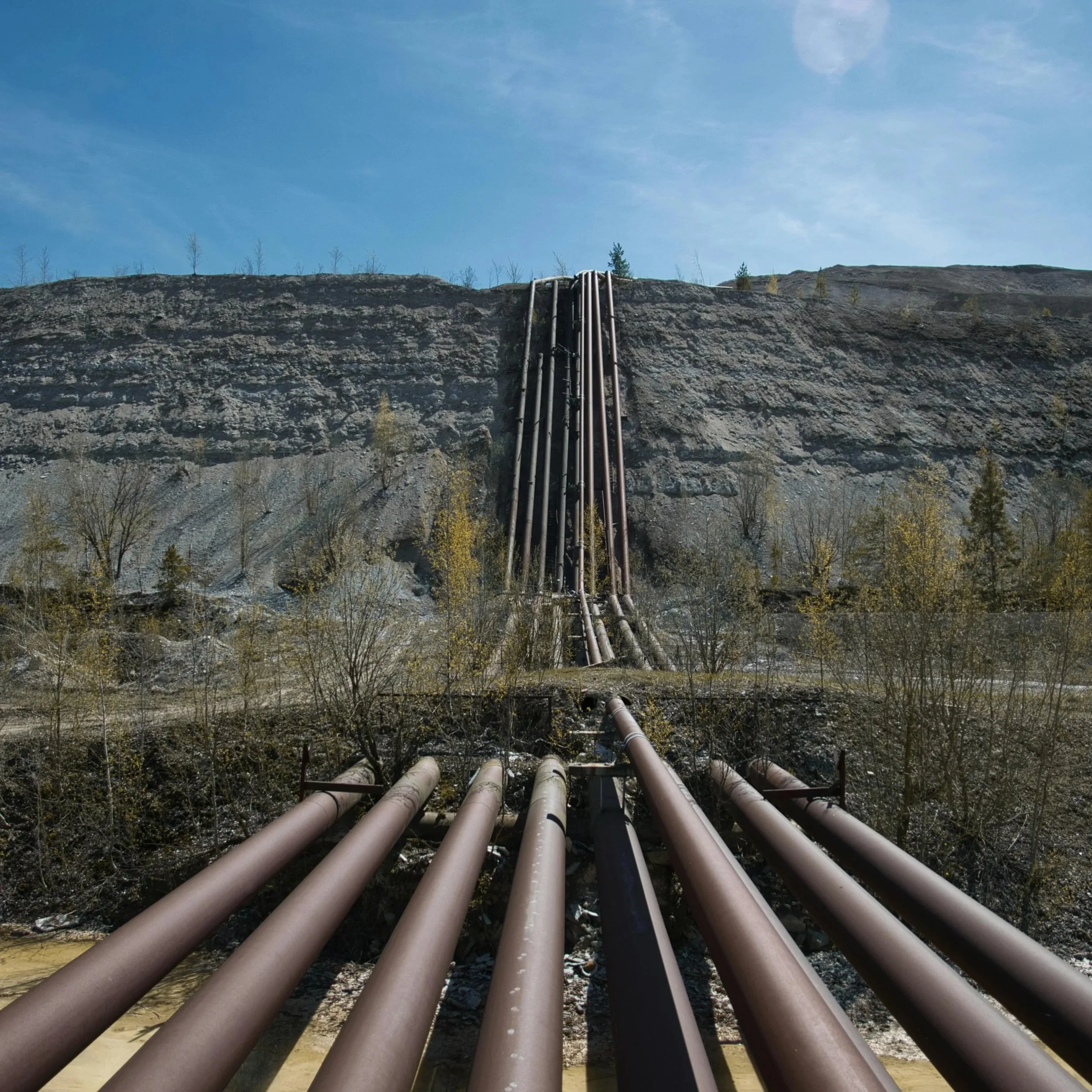 Multiple pipelines extending into the distance and running up a hillside, forming a network across the sloped terrain.
