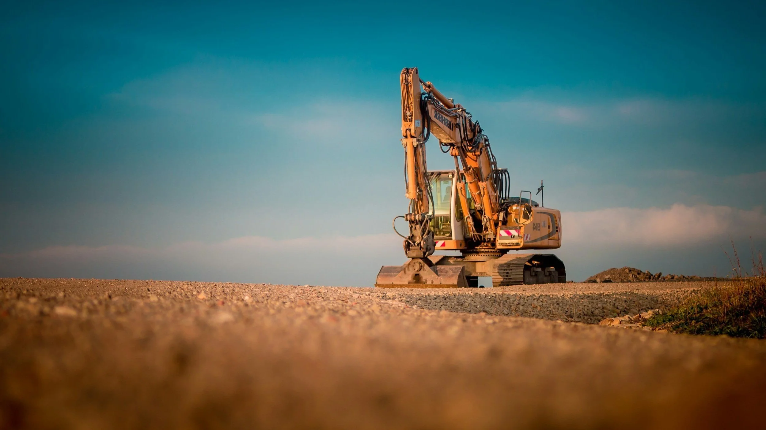 Construction site featuring a yellow excavator parked on bare ground, surrounded by building materials and construction equipment.