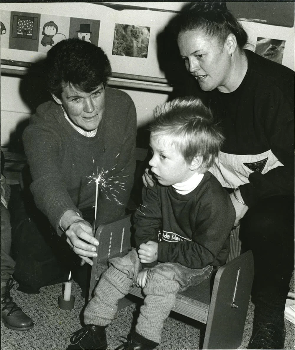 A woman and two men are helping a young boy light a sparkler during a celebration or event